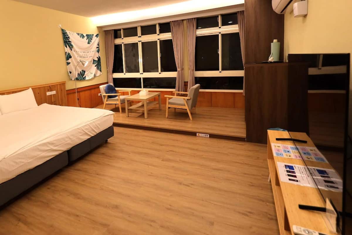 A hotel room with a bed, a desk, a chair, a window, and a tapestry.