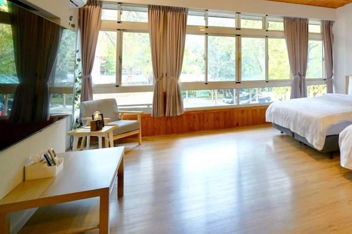 A hotel room with two beds, a wooden floor, a desk, and large windows with curtains.