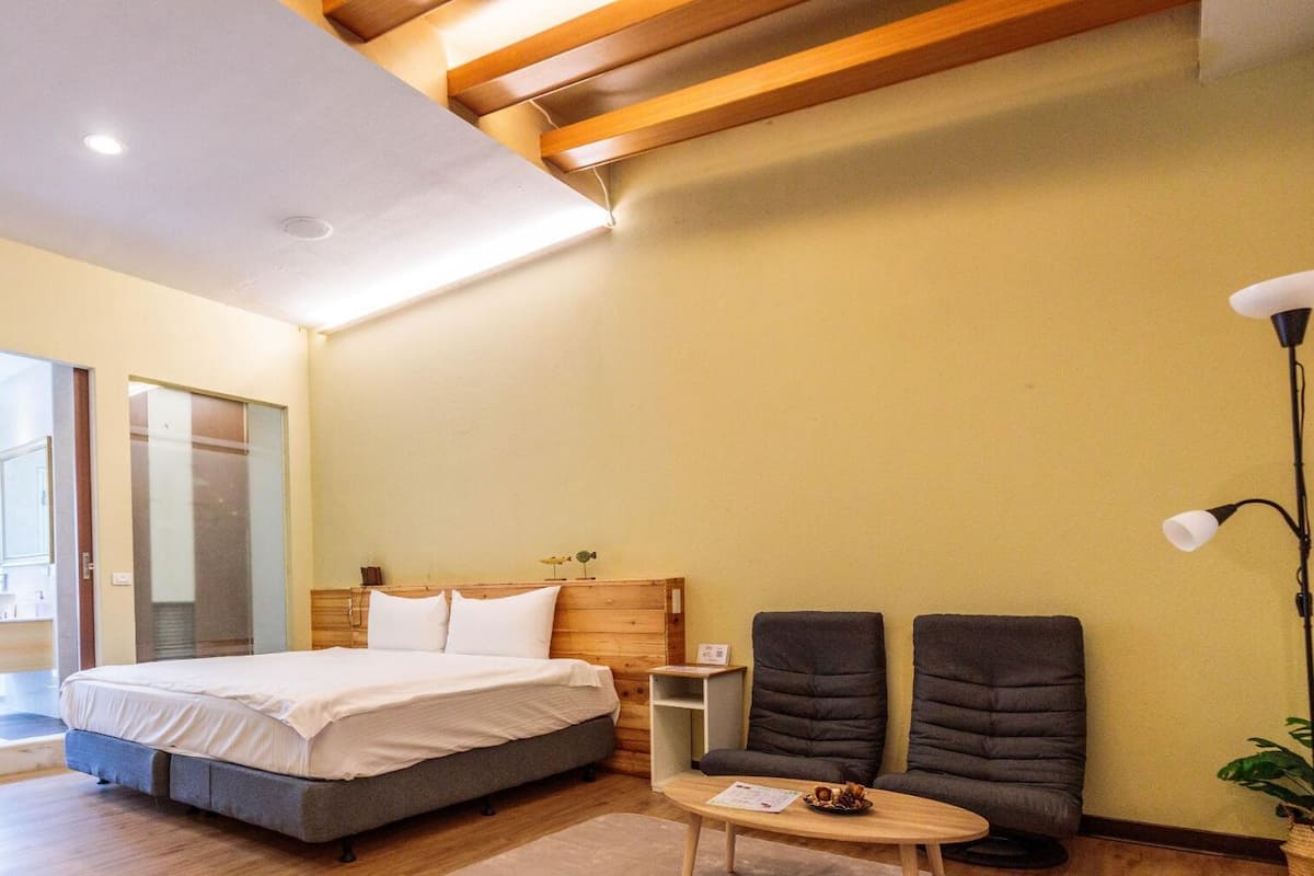 A hotel room with a bed, a small table, two armchairs, and a nightstand.