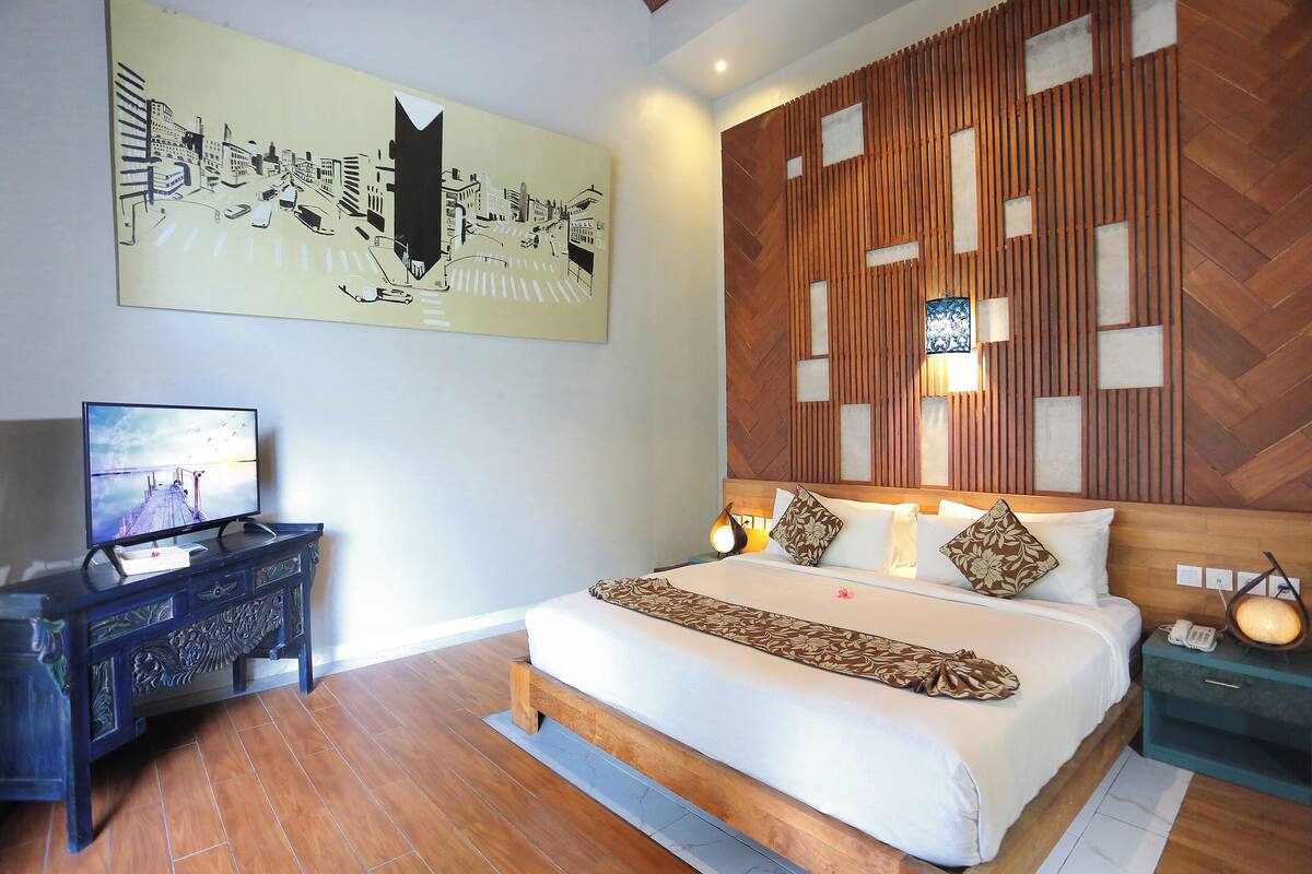 Une chambre d’hôtel avec un lit, une télévision, une tête de lit en bois et un tableau représentant un paysage urbain.