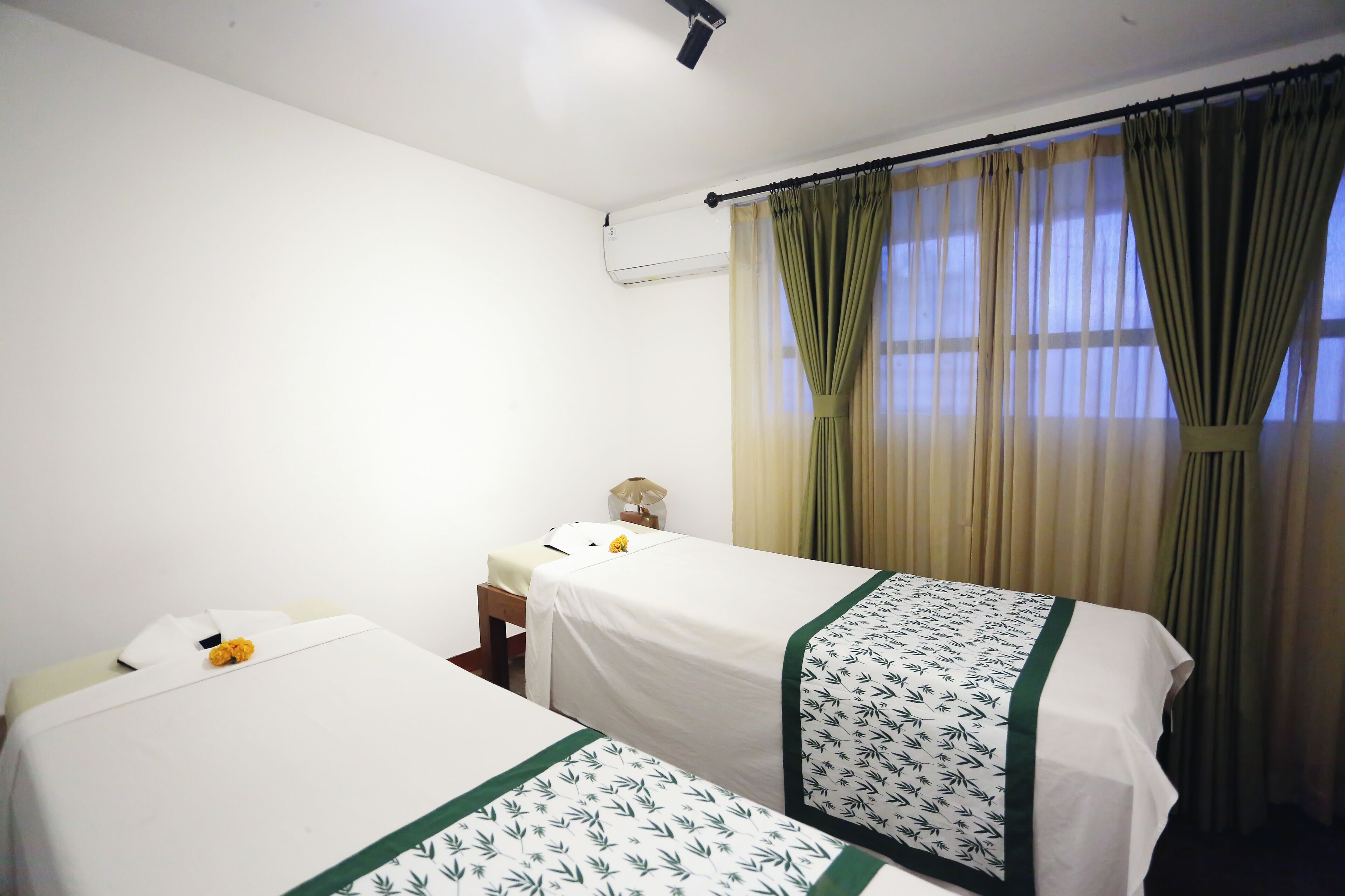 A hotel room with two single beds, a small bedside table, a lamp, and a window with curtains.