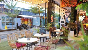 Ein Straßencafé mit Korbstühlen und Tischen, eine Bar im Hintergrund und Blick auf die Straße.