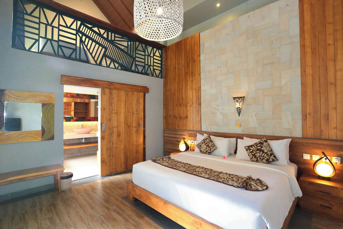 Une chambre spacieuse avec un grand lit, une tête de lit en bois et un luminaire moderne.