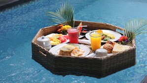 Ein schwimmendes Tablett mit Frühstücksangeboten über einem Pool, umgeben von üppiger Vegetation.