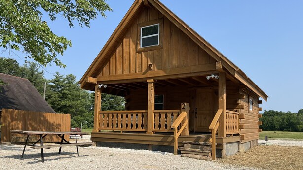 A wooden cabin with a porch, a picnic table, and a fire pit.