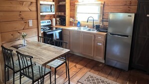 A compact kitchen with wooden cabinets, a stainless steel refrigerator, a sink, and a dining area with a table and chairs.