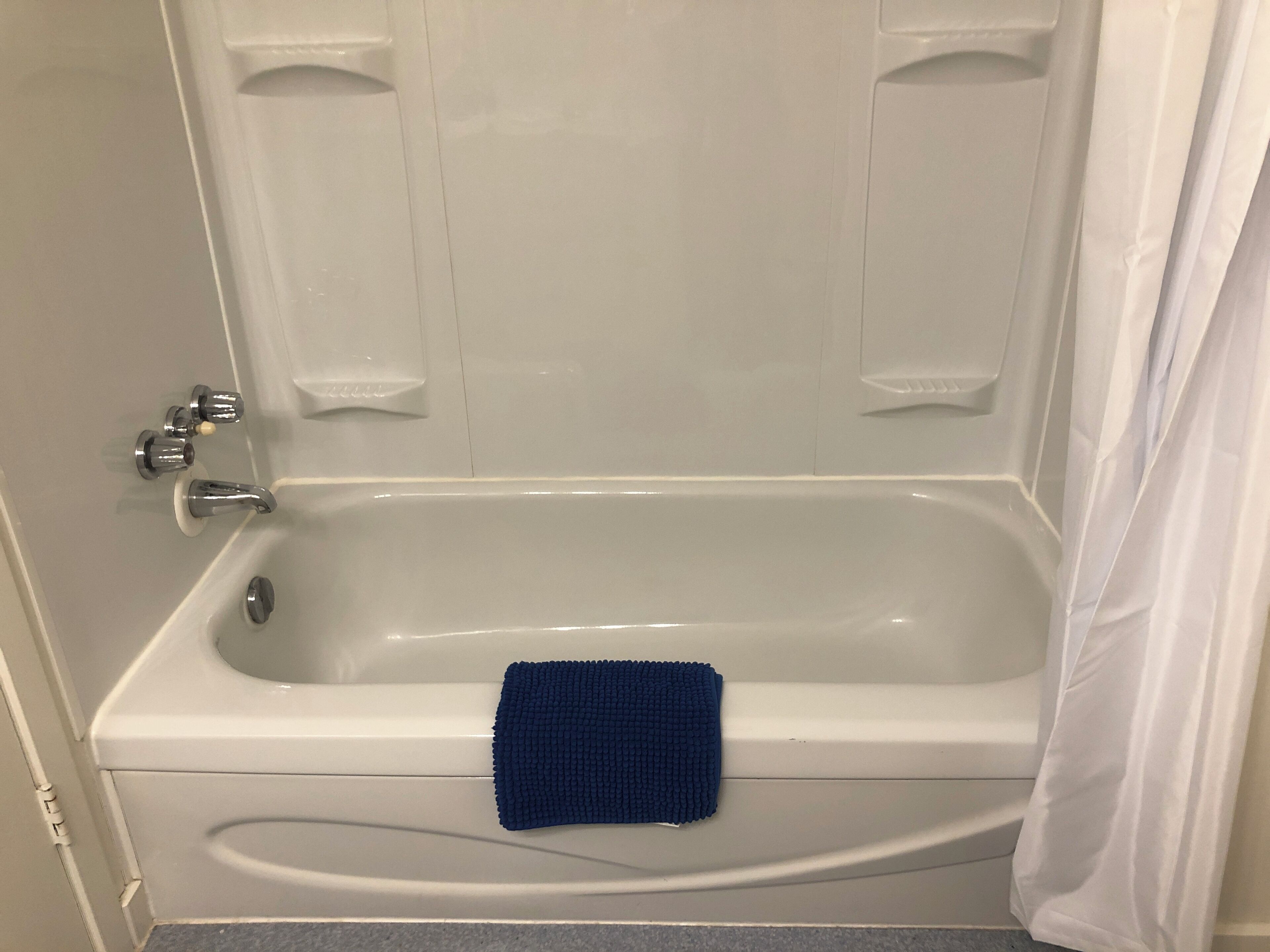 Une baignoire blanche, une serviette bleue, un rideau de douche et un robinet.