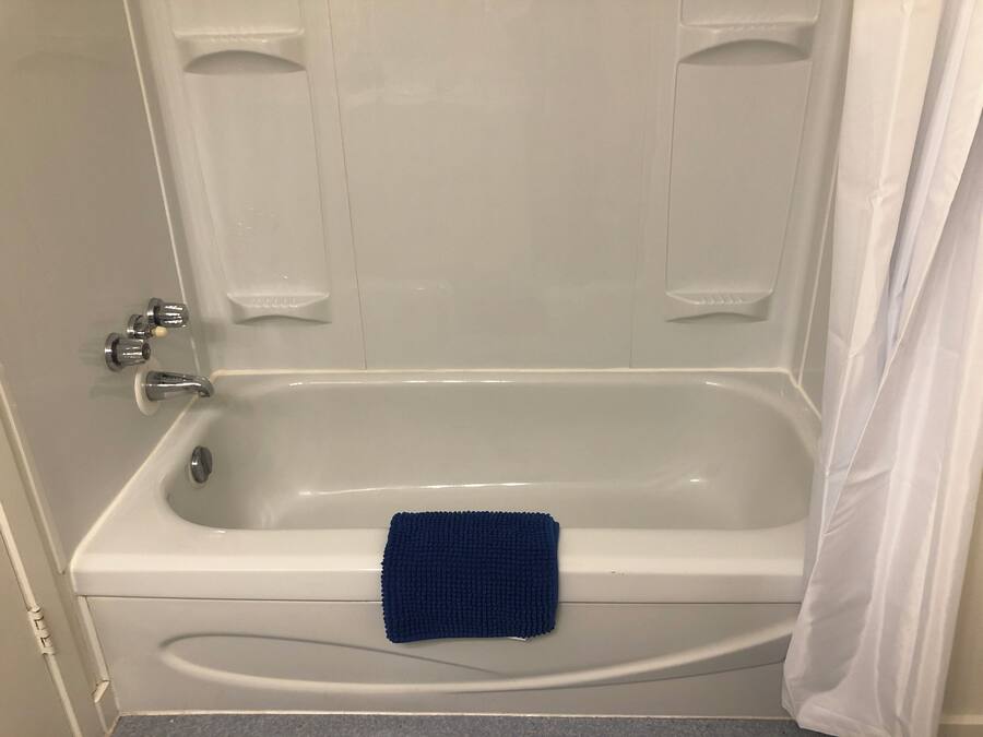 Une baignoire blanche, une serviette bleue, un rideau de douche et un robinet.