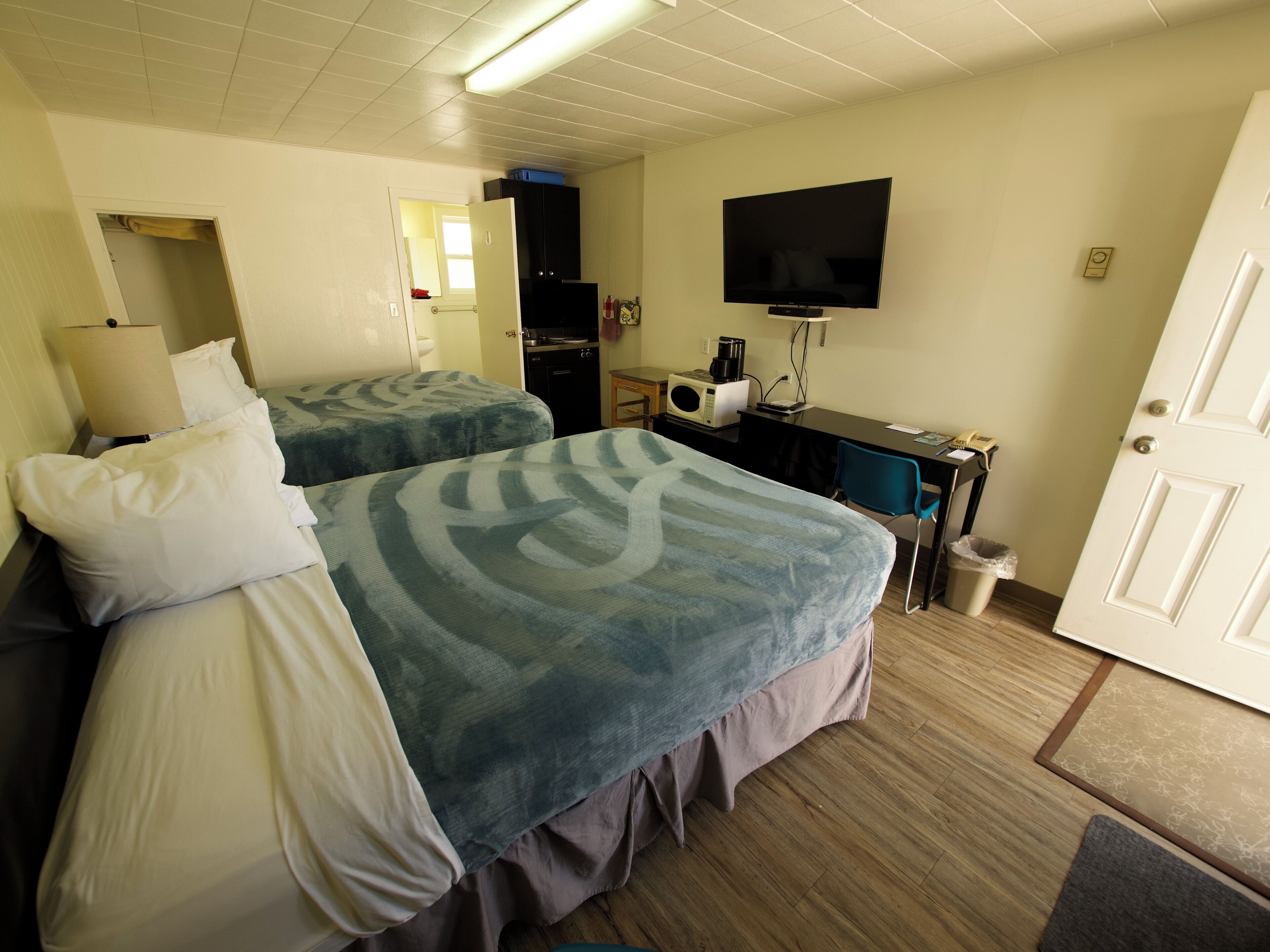 A hotel room with two beds, a desk with a computer, a TV, and a microwave.