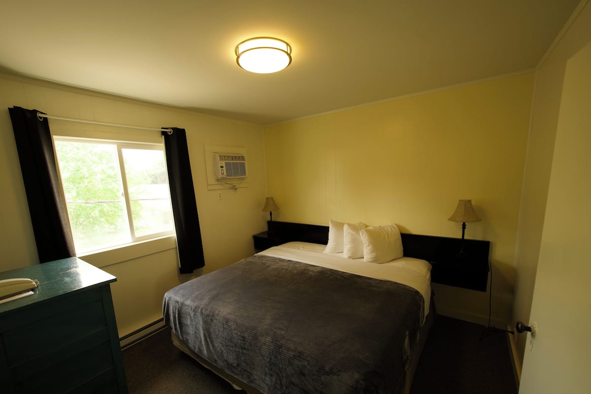 Quarto com cama, escrivaninha, janela com cortinas e luminária de teto.