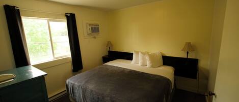 A bedroom with a bed, a desk, a window with curtains, and a ceiling light.