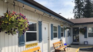 Un motel con dos bancos de madera afuera, un letrero que dice 'NO INGRESAR EN REVERSA' y cestas de flores colgando del toldo.