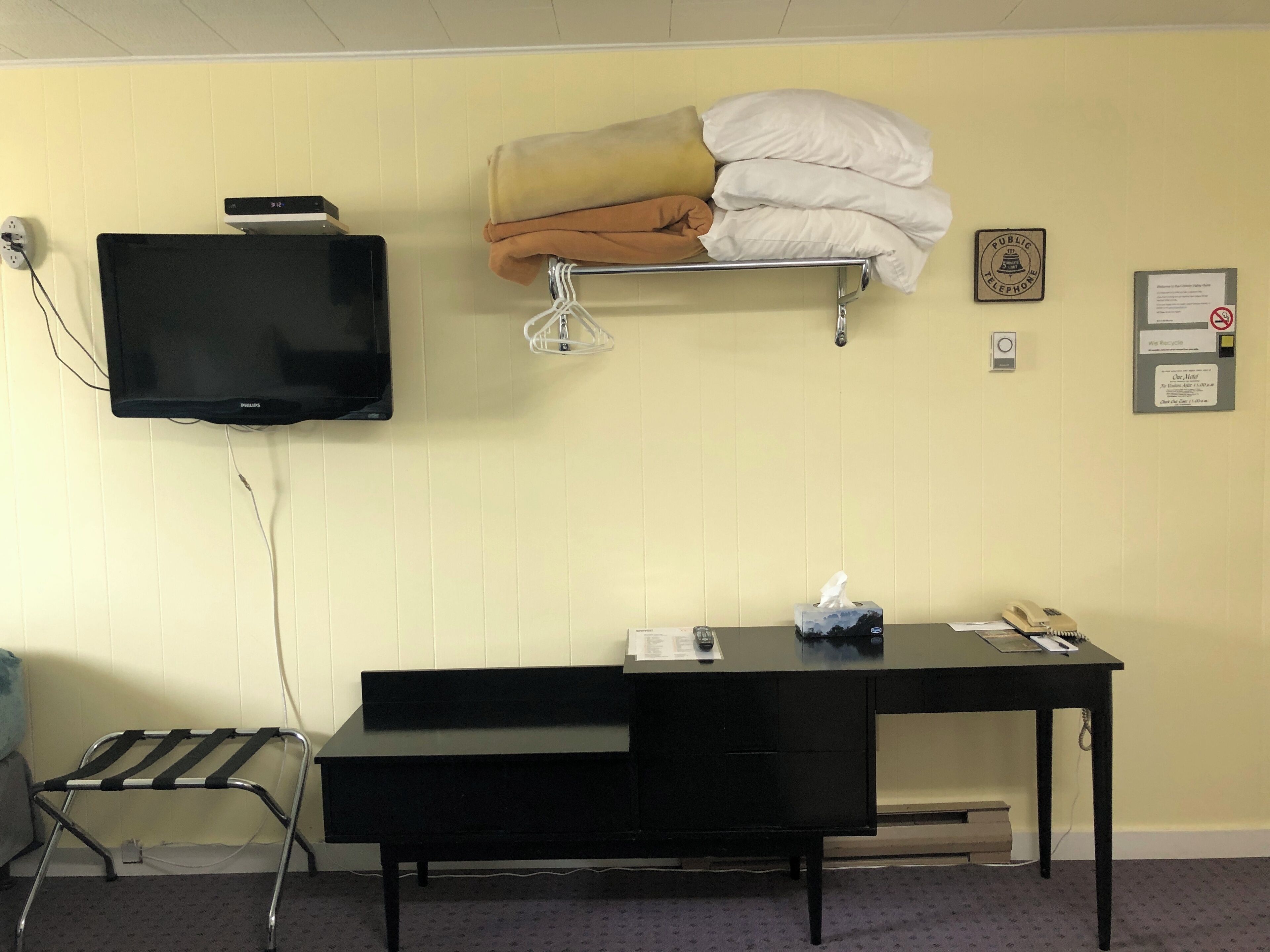 Une chambre d’hôtel équipée d’un lit, d’un bureau, d’une télévision, d’un téléphone et d’une étagère fixée au mur avec des oreillers.