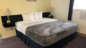 Habitación de hotel con cama, dos mesitas de noche con lámparas, una obra de arte en la pared y una ventana con cortinas.