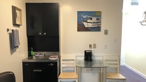 Una cocina compacta con lavavajillas, cafetera y un cuadro de un barco en la pared.