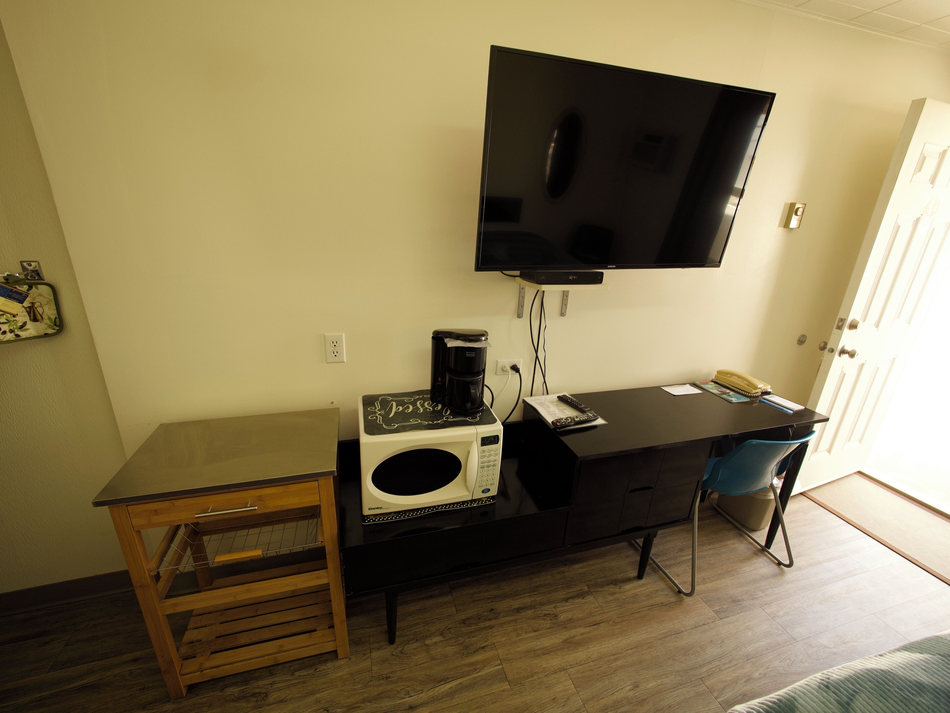 Quarto compacto com escrivaninha, micro-ondas, máquina de café, televisão e uma cadeira.