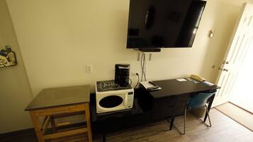 Quarto compacto com escrivaninha, micro-ondas, máquina de café, televisão e uma cadeira.