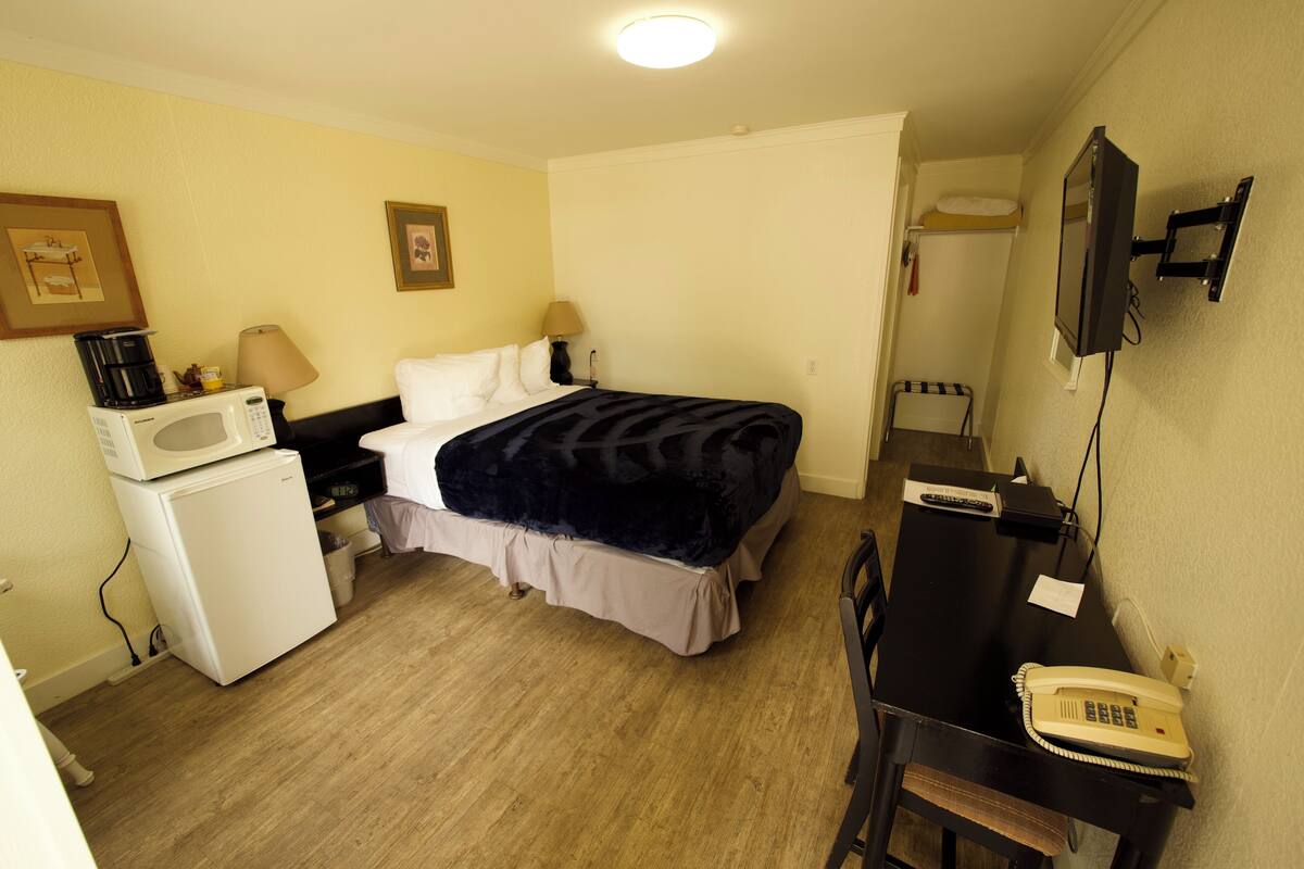 Quarto de hotel pequeno com uma cama, uma escrivaninha com telefone, micro-ondas e um frigorífico.