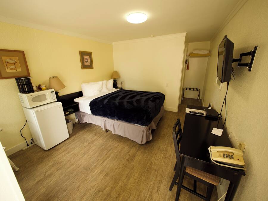 A compact hotel room with a bed, a desk with a telephone, a microwave, and a small refrigerator.