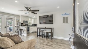 Ein modernes Wohnzimmer mit einer Couch, einem Essbereich mit Tisch und Stühlen, einer Küche im Hintergrund und einem Deckenventilator.
