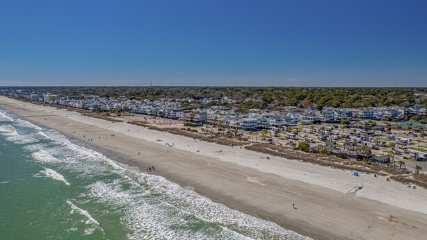 Luftaufnahme einer Küstenstadt mit Strand, Häusern und blauem Himmel.