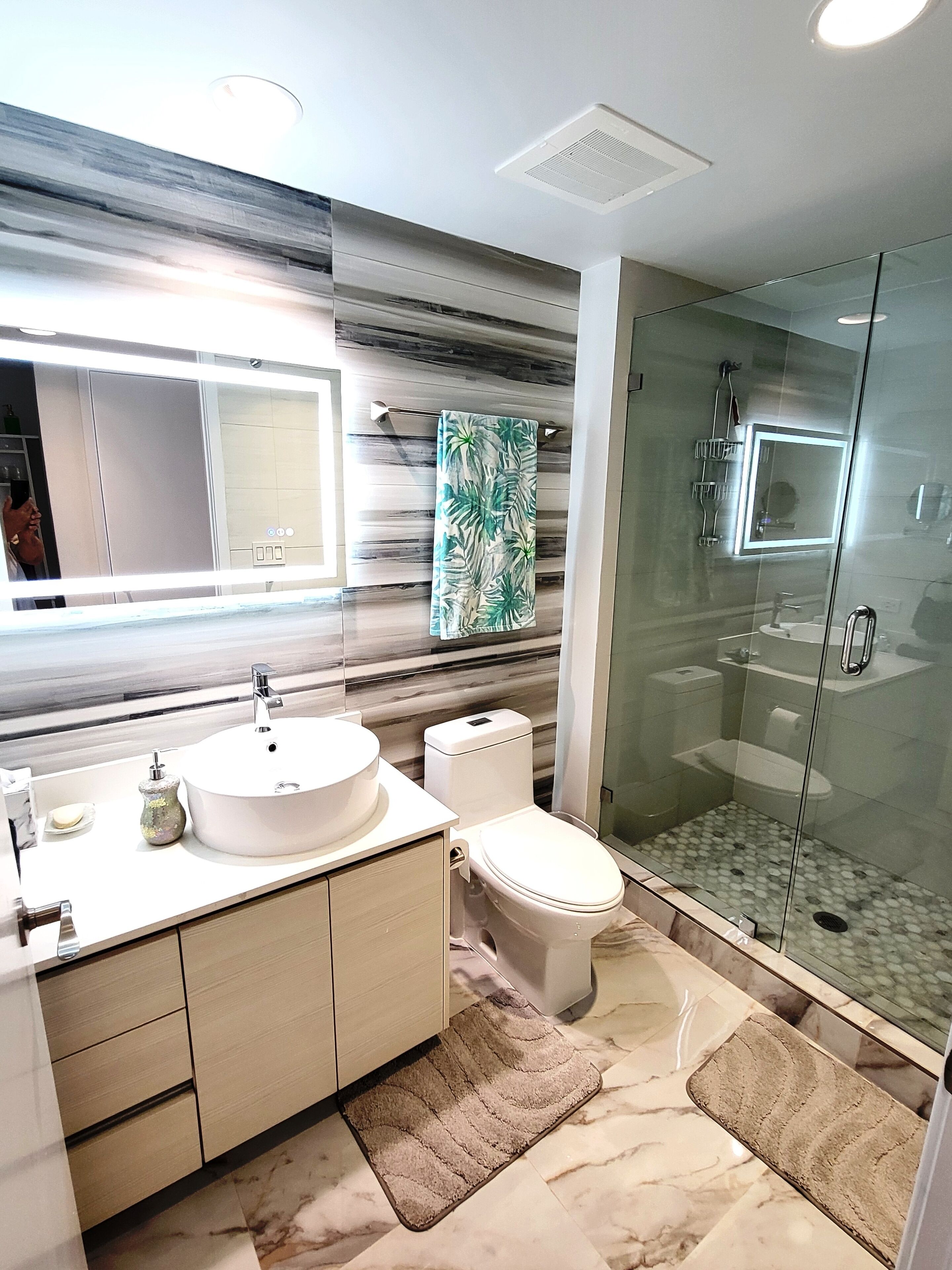 A modern bathroom with a large mirror, a round sink, a toilet, and a glass-enclosed shower.