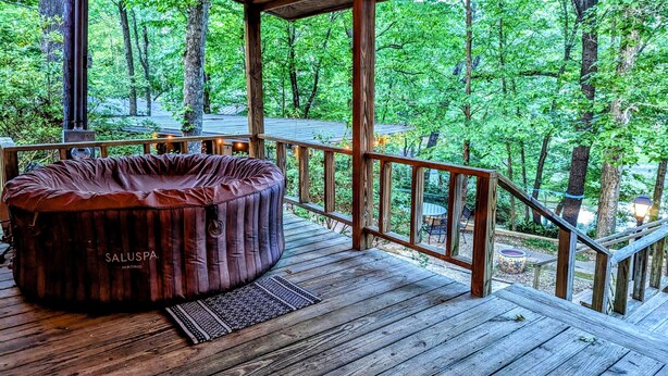 Um deck de madeira com hidromassagem, cercado por grades de madeira, com vista para uma área arborizada.