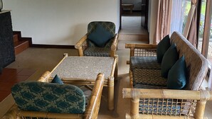 Una habitación con mobiliario de mimbre, una lámpara colgante y vistas a un jardín a través de amplios ventanales.