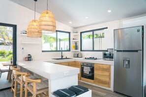 A modern kitchen with white cabinetry, a stainless steel refrigerator, a built-in oven, and a large island with bar stools.