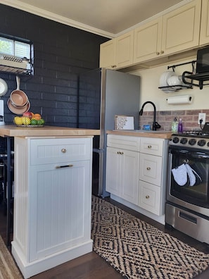 A kitchen with white cabinets, a black brick wall, a stainless steel oven, and a patterned rug.