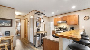 Una cocina con armarios de madera, un refrigerador de acero inoxidable, una isla de madera con taburetes de bar y un reloj en la pared.