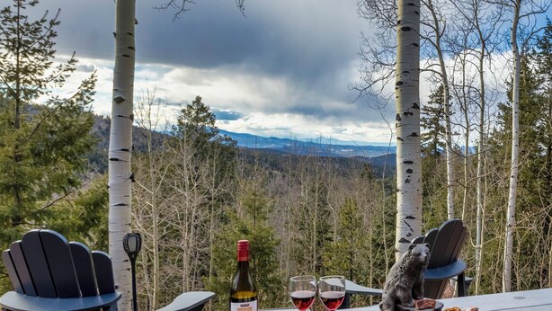 Una mesa servida con queso, pan y vino, con una vista panorámica de montañas al fondo.