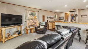 Sala de estar con televisor, sofá de cuero, mesa de centro de madera y una zona de cocina con barra.