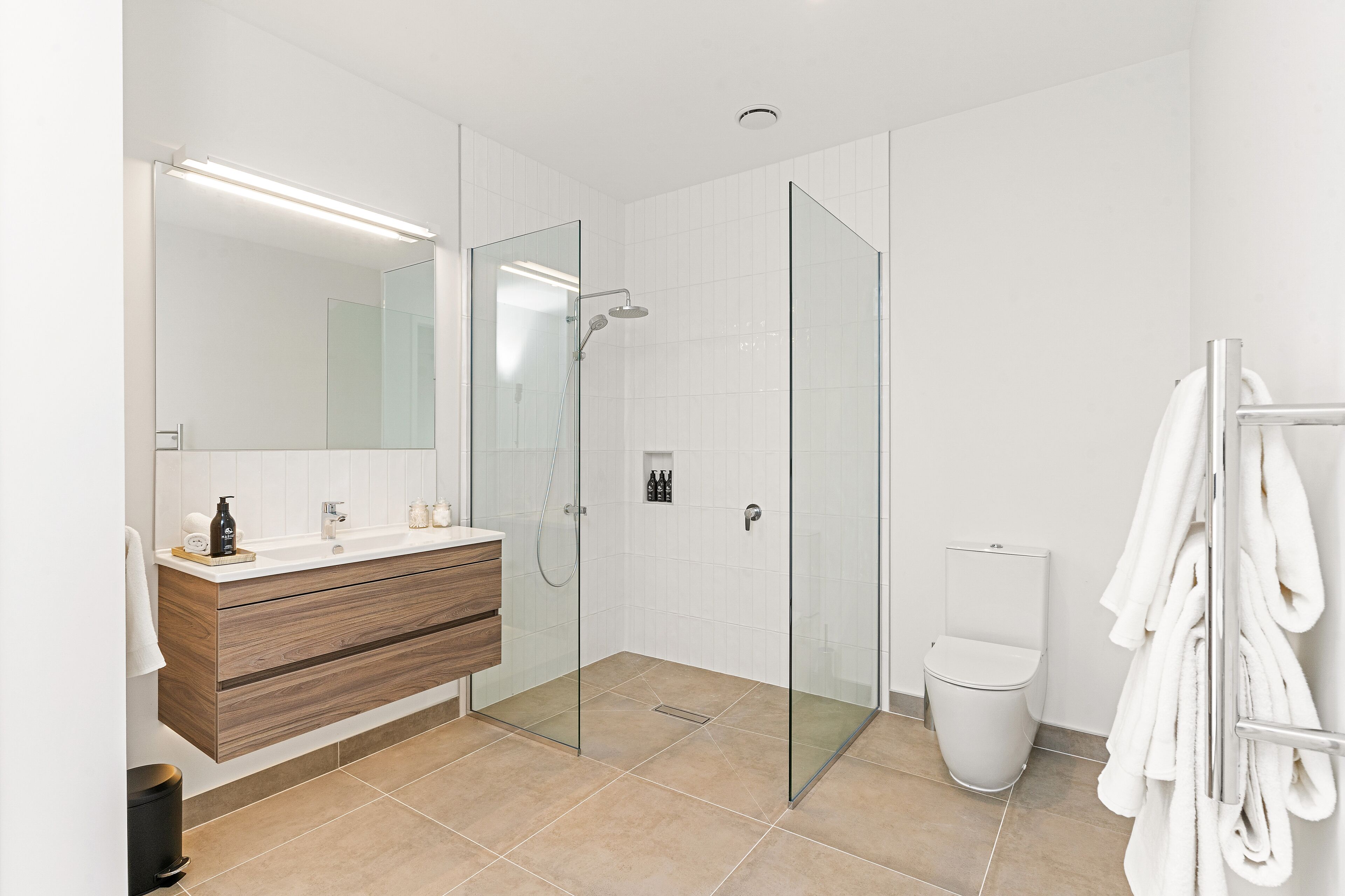 Un baño moderno con ducha de vidrio, tocador de madera, inodoro y perchero para toallas.