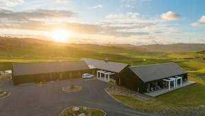 A modern building with a covered outdoor seating area and a paved driveway. - Te Karaka Lodge (Waikaretu)