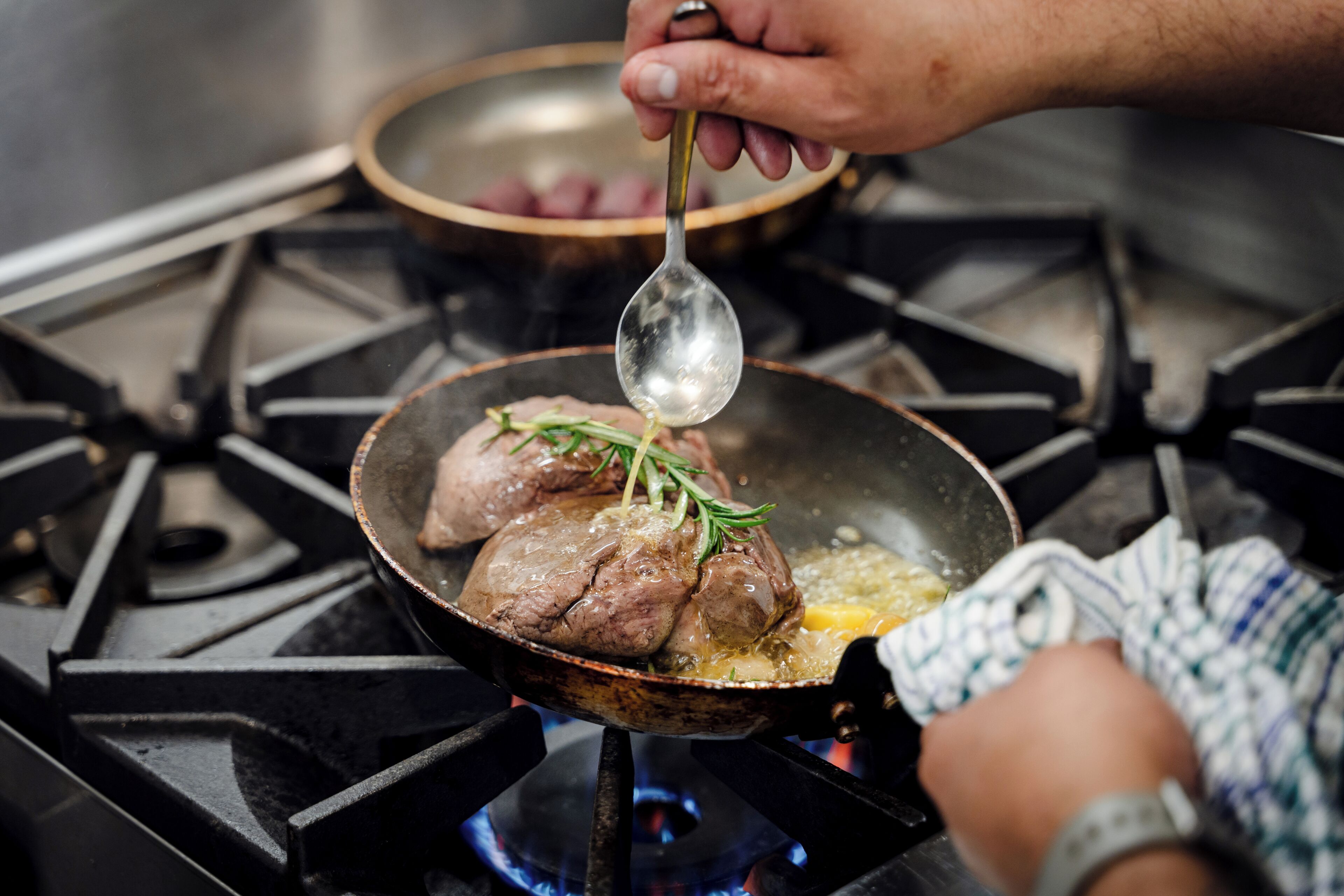 A person cooking meat in a pan on a stove.