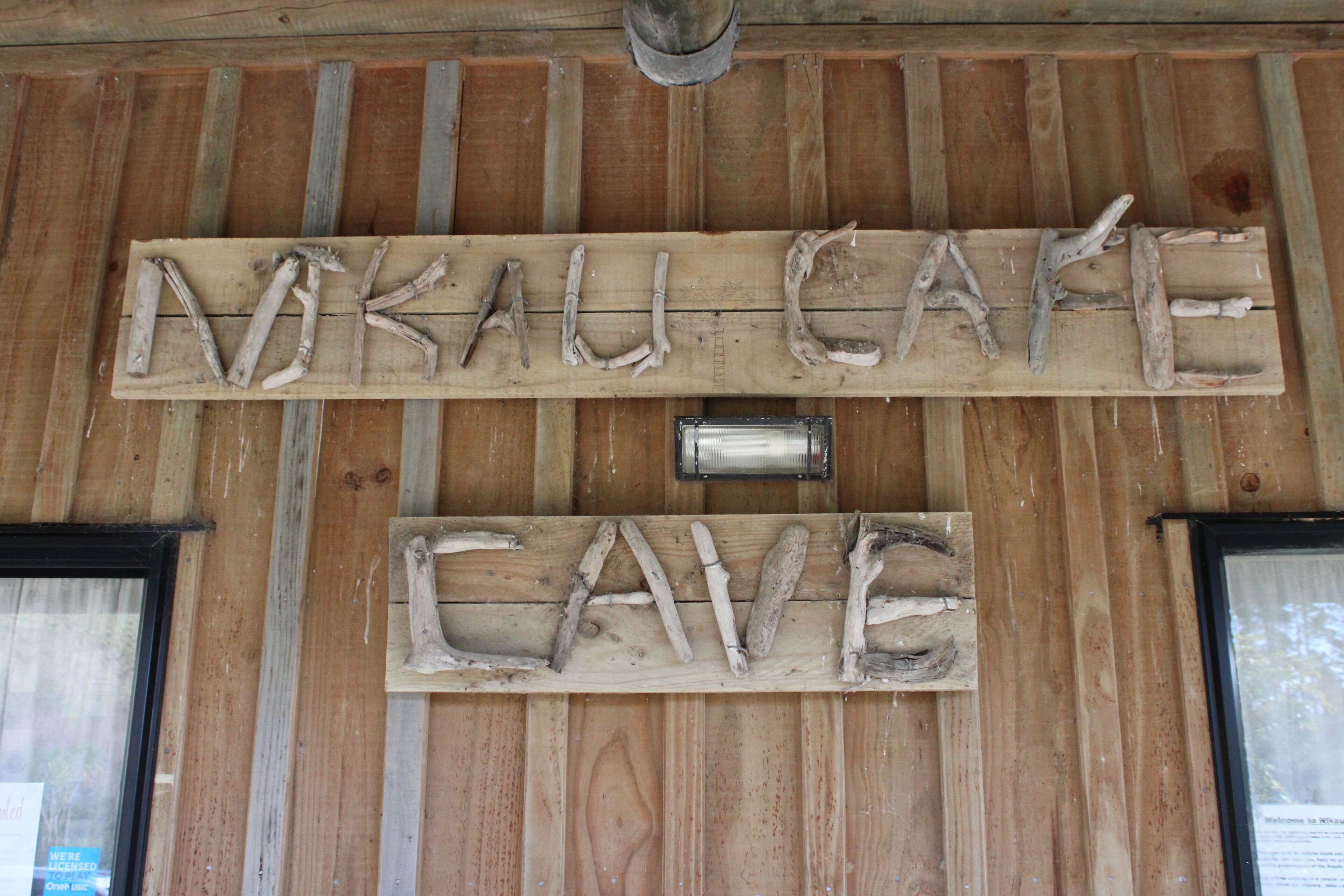 Een houten bord met de tekst 'Nkau Cafe' en 'Cave' erin gebeiteld, bevestigd aan een houten muur.
