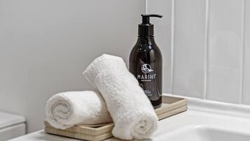 A bathroom with a white bathtub, a black bottle of Marijke Aoteaqua body wash, and two white towels on a wooden tray.