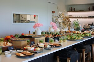 Una mesa de buffet con diversos alimentos y bebidas, incluyendo frutas, quesos y ensaladas.