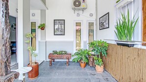 A clean, well-lit hallway with a bench, potted plants, and a mounted air conditioning unit. - Hotel O Homestay Grand Mahkota Permai Syariah (Muncar)