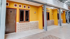 A building with a yellow exterior, numbered doors, and a tiled entrance area. - Hotel O Amole Paviliun Syariah (Cilacap)