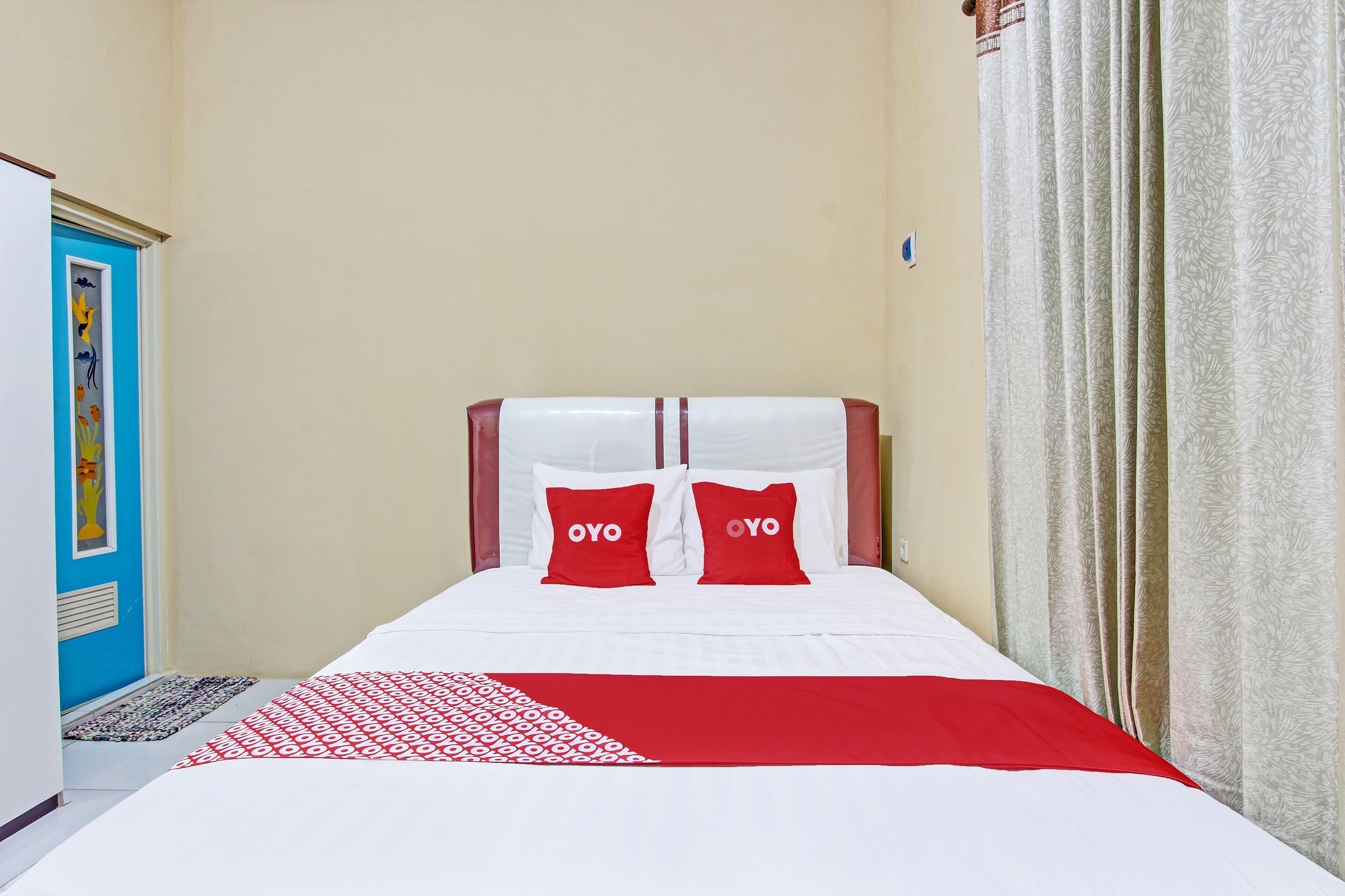 Une chambre d’hôtel avec un lit, deux oreillers rouges ornés du texte « OYO », un couvre-lit blanc et un plaid rouge et blanc à motifs.