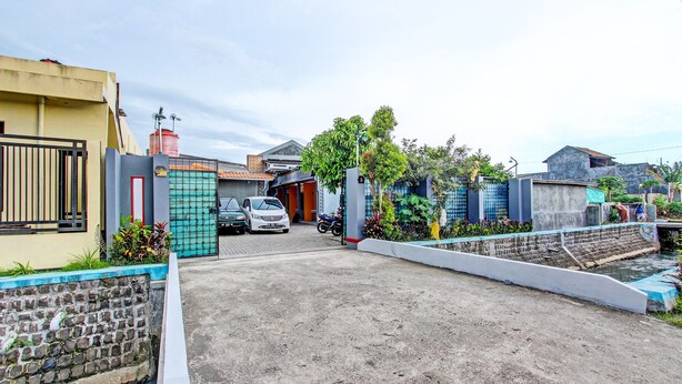 A residential area with a gated entrance, parked cars, and a small water feature. - Hotel O Amole Paviliun Syariah (Cilacap)