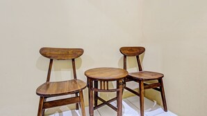 Three wooden chairs with a round table in between, positioned against a plain wall. - Hotel O Amole Paviliun Syariah (Cilacap)