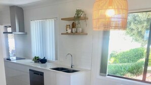 Een moderne keuken met witte kasten, een inbouw vaatwasser, en een eethoek met een witte tafel en stoelen.