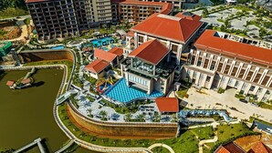 Vista aérea de un hotel con piscina, un edificio grande con techo rojo y un área ajardinada circundante.