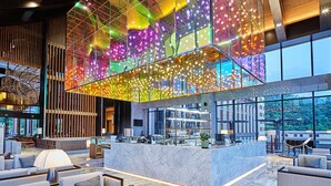 Un moderno vestíbulo de hotel con techo de cristal, zonas de estar y una recepción.
