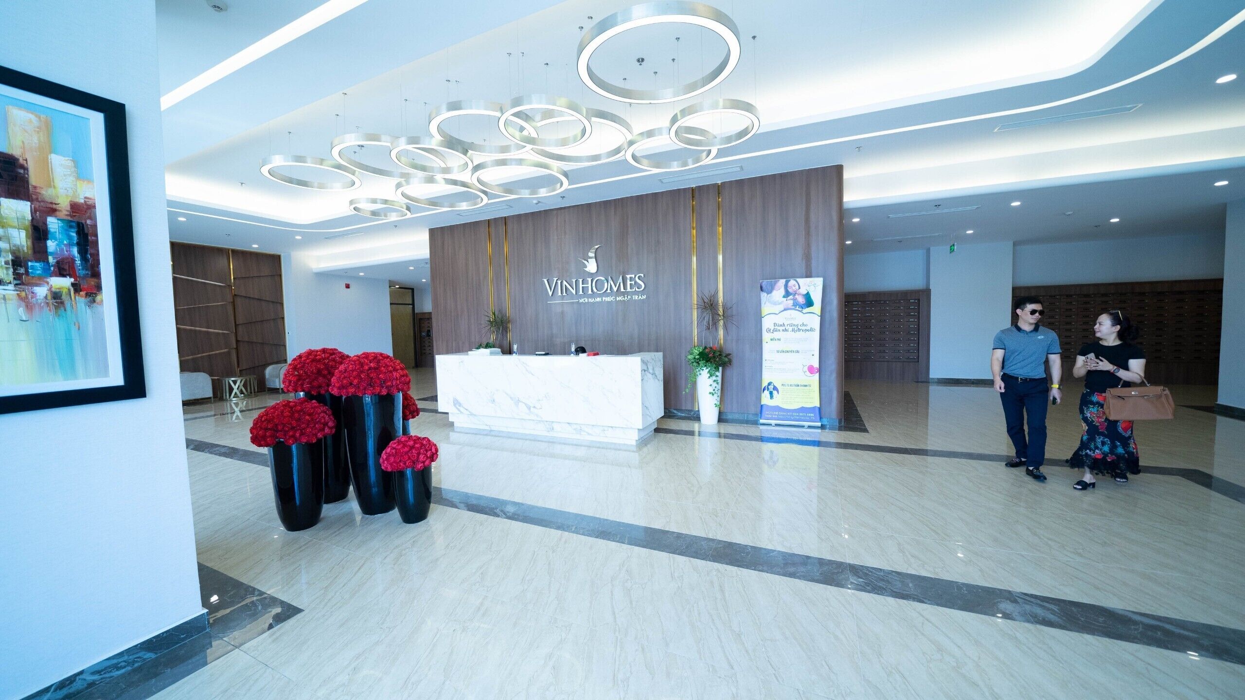 A reception area with a modern design, featuring a marble reception desk, a logo on the wall, and a large floral arrangement.