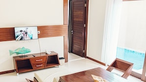 Un comedor moderno con una mesa y sillas de madera, un televisor montado en la pared y vistas al mar a través de amplias ventanas.