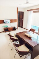 Un comedor moderno con una mesa y sillas de madera, un televisor montado en la pared y vistas al mar a través de amplias ventanas.